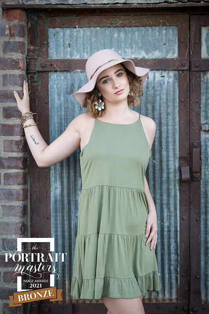 Photo of a high school senior girl wearing a pink hat and a green dress which received a Bronze Merit at the 2021 Portrait Masters Awards