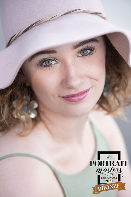 Photo of a high school senior girl wearing a pink hat and a green dress which received a Bronze Merit at the 2021 Portrait Masters Awards