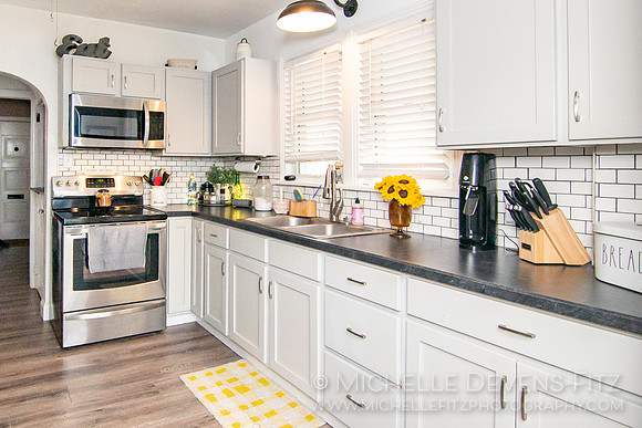 Kitchen with white cabinets, black counter tops, and laminate flooring.
